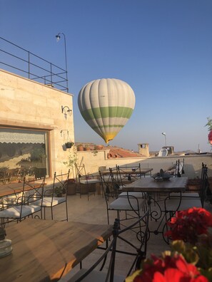 A rooftop terrace with outdoor seating, a hot air balloon in the background, and a clear sky. - Ikarus Cappadocia Hotel (Nevsehir)