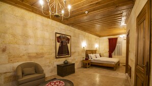 A room with a bed, a chair, a small table with a decorative plate, a wall-mounted lamp, and a chandelier. - Ikarus Cappadocia Hotel (Nevsehir)