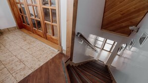 A wooden staircase with a handrail, leading to a room with a tiled floor and a wooden door with glass panels. - Casa Jainen (Ushuaia)