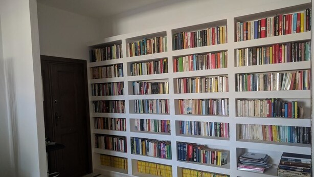 Una habitación con una amplia estantería llena de libros, una puerta y un piso con baldosas.