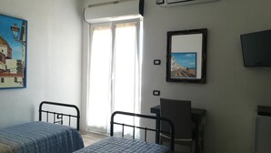 Una habitación con dos camas, un escritorio, una silla, un televisor y una ventana con cortinas.