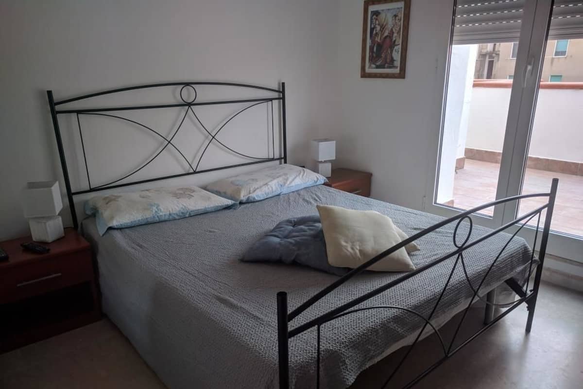 Una camera da letto con una struttura letto in metallo, un letto singolo con copripiumino grigio e bianco, due comodini con lampade e una finestra con persiane.