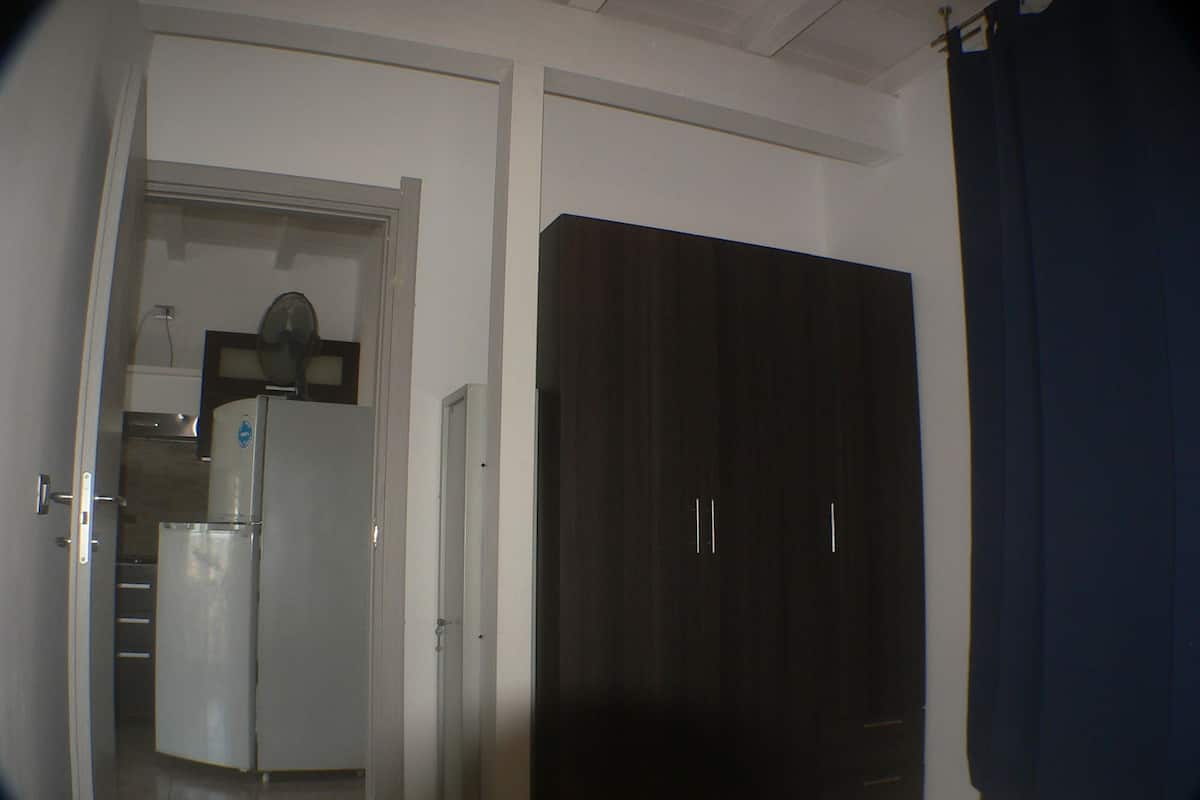 Una stanza con un armadio scuro, una porta bianca e un angolo cottura dotato di frigorifero e microonde.