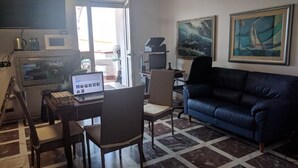 Una sala de estar con una laptop sobre una mesa, un sofá azul y dos cuadros en la pared.