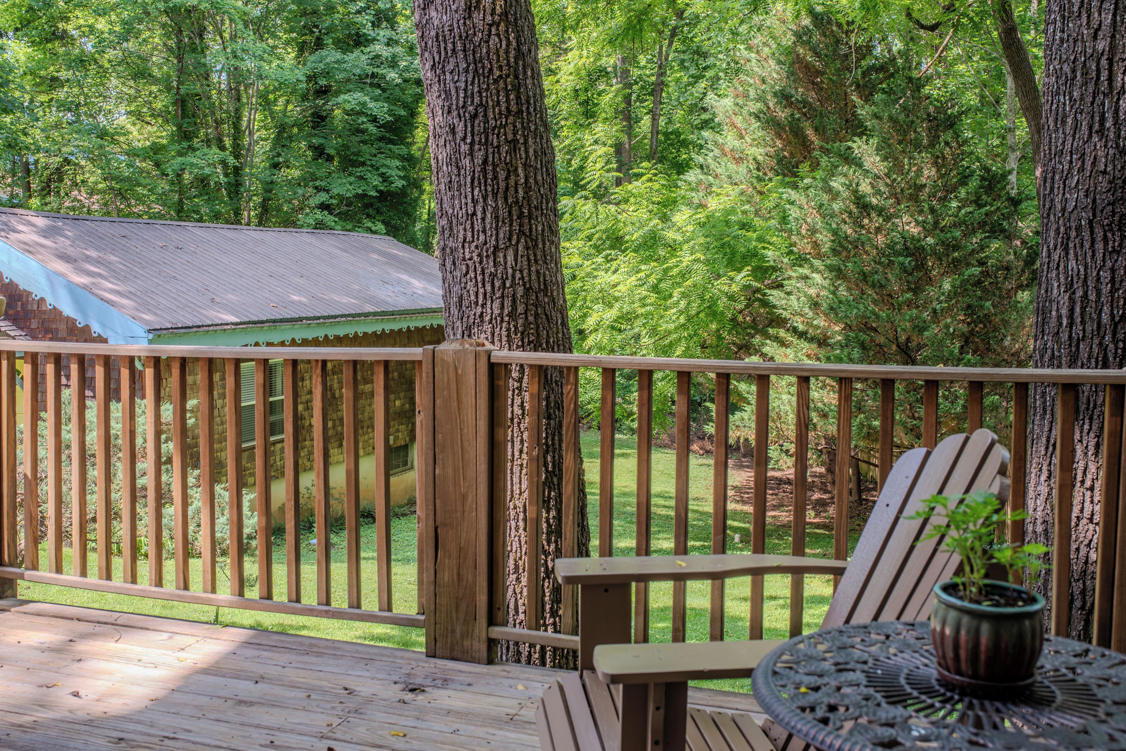 A wooden deck with a railing, a table with a potted plant, and a green-roofed building in the background.