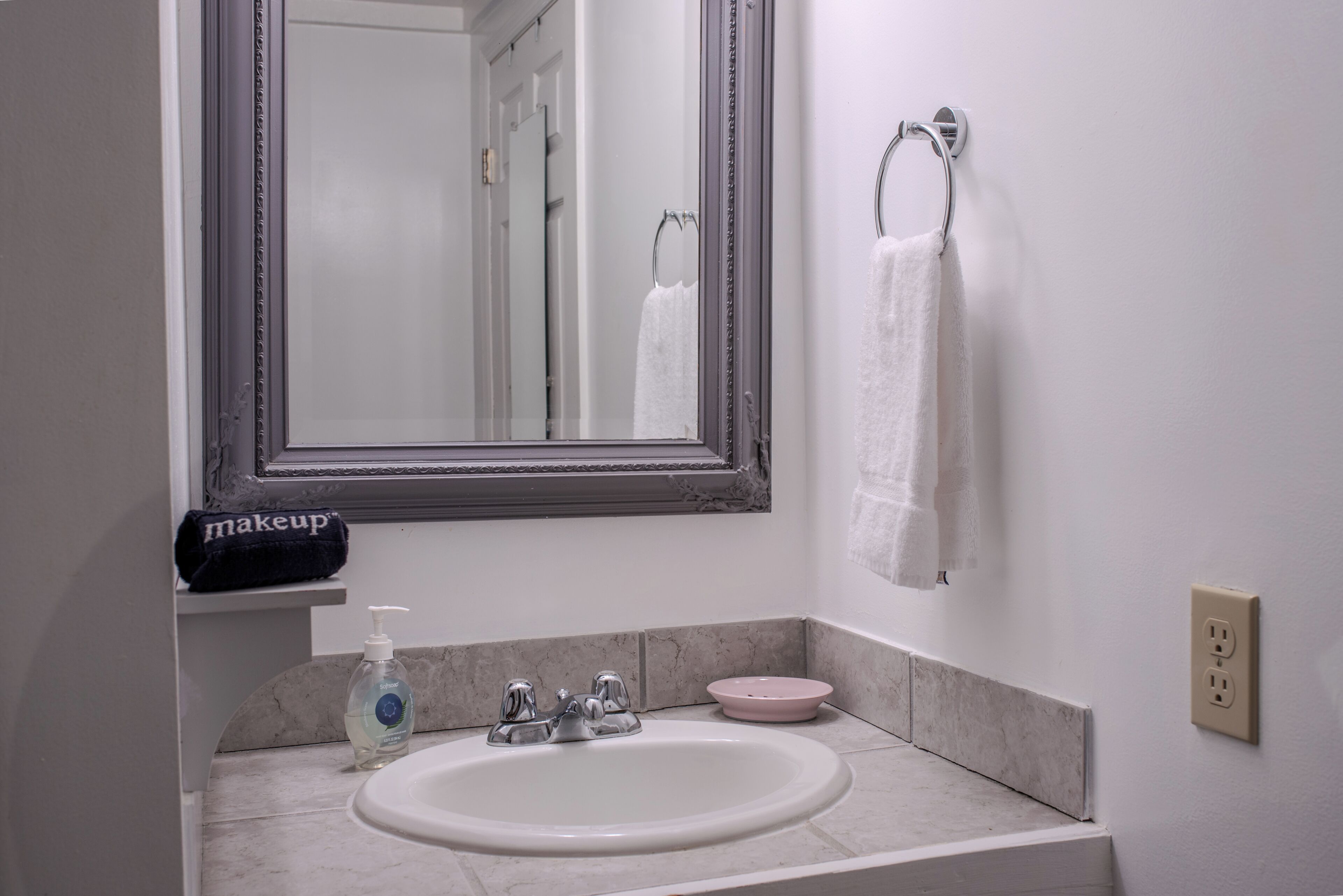 A bathroom with a white sink, a mirror, a towel rack, a makeup towel, and a soap dispenser.