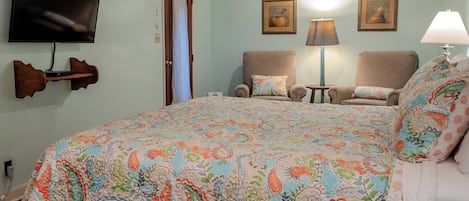 A bedroom with a large bed, two armchairs, a TV mounted on the wall, and a door.