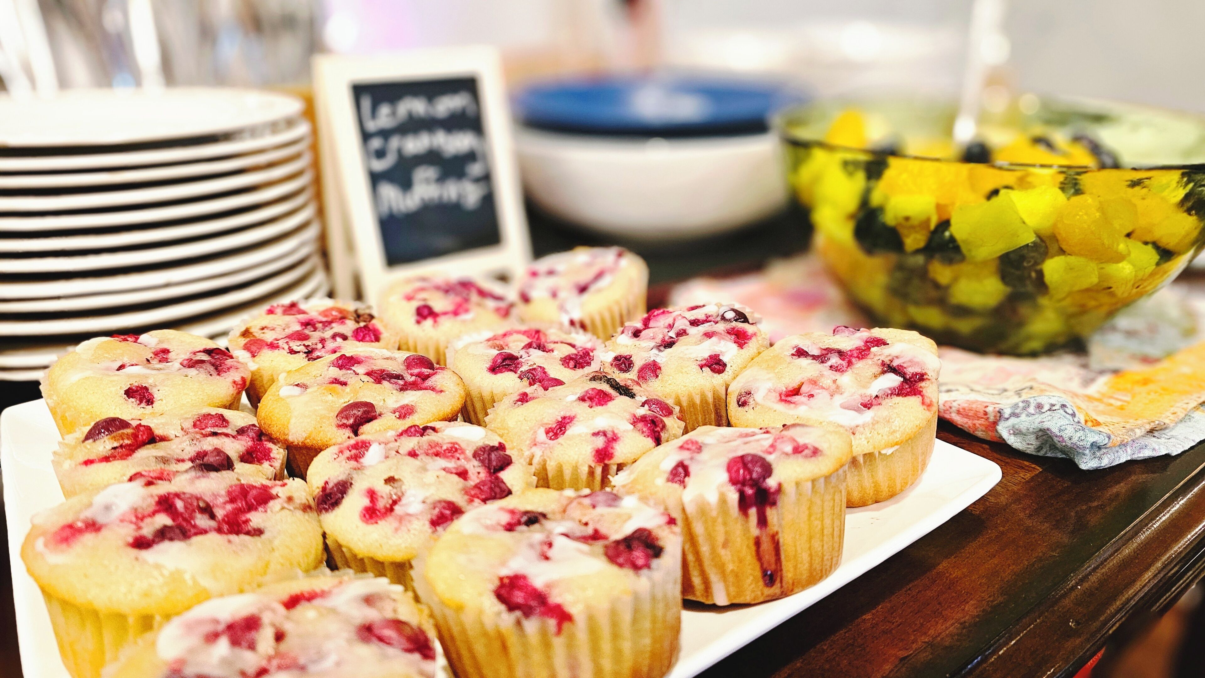 A table with a plate of muffins topped with fruit and a sign reading 'Lemon Cranberry Muffins'.
