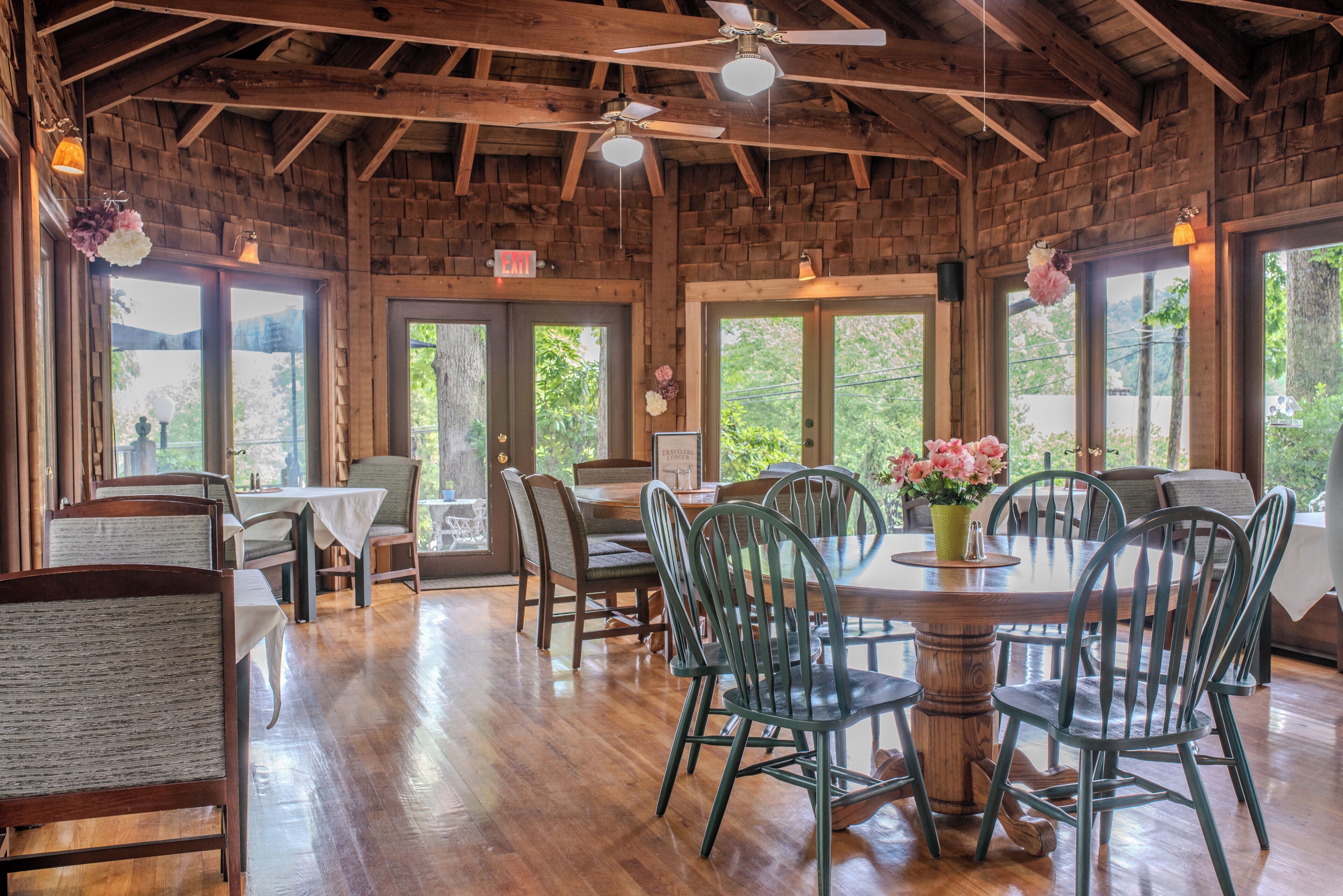 A restaurant with wooden walls, large windows, and a central dining table surrounded by chairs.