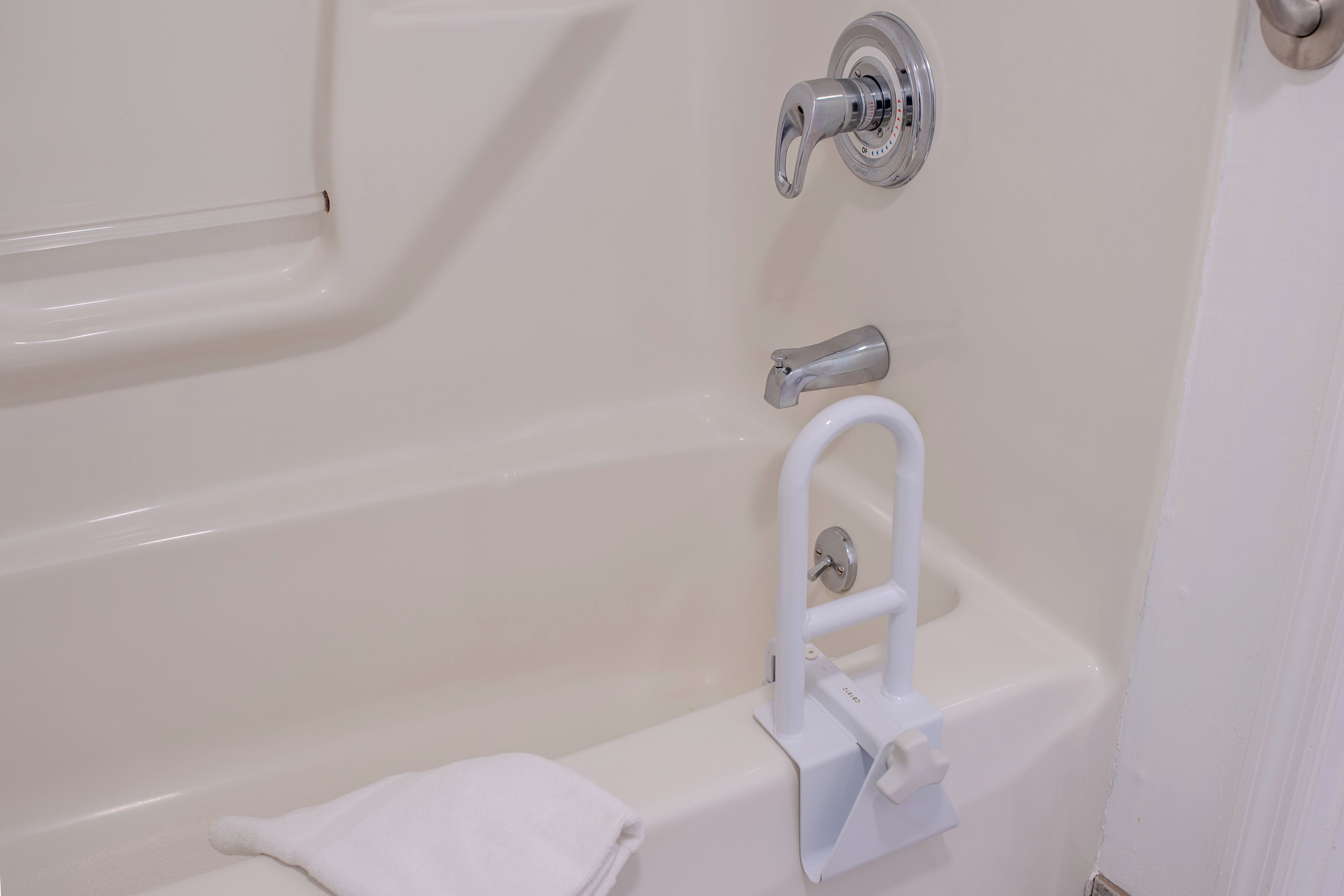 Une baignoire équipée d’un pommeau de douche à main, d’une barre d’appui et d’une serviette posée sur le sol.