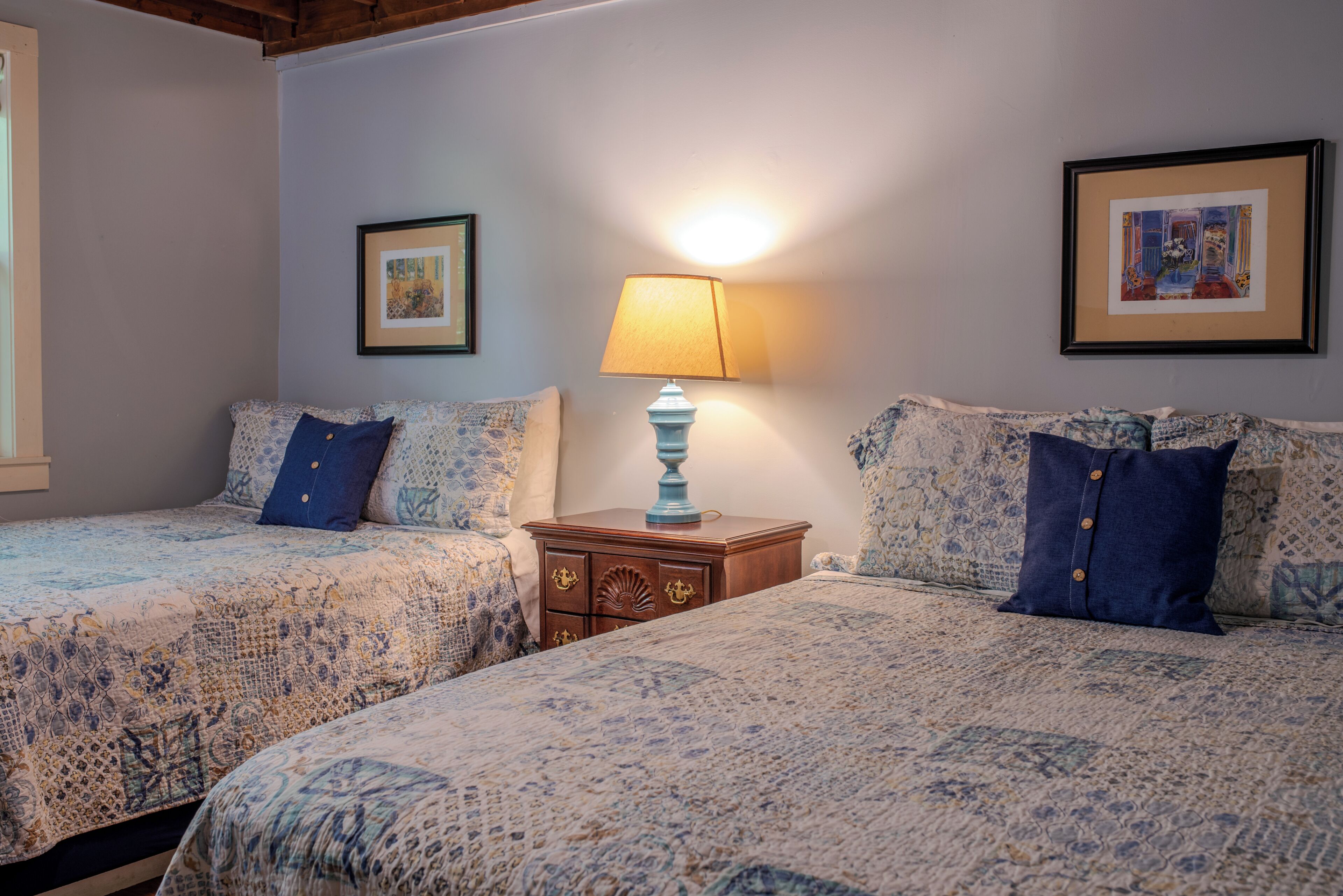 A bedroom with two beds, a nightstand, and framed pictures on the wall.