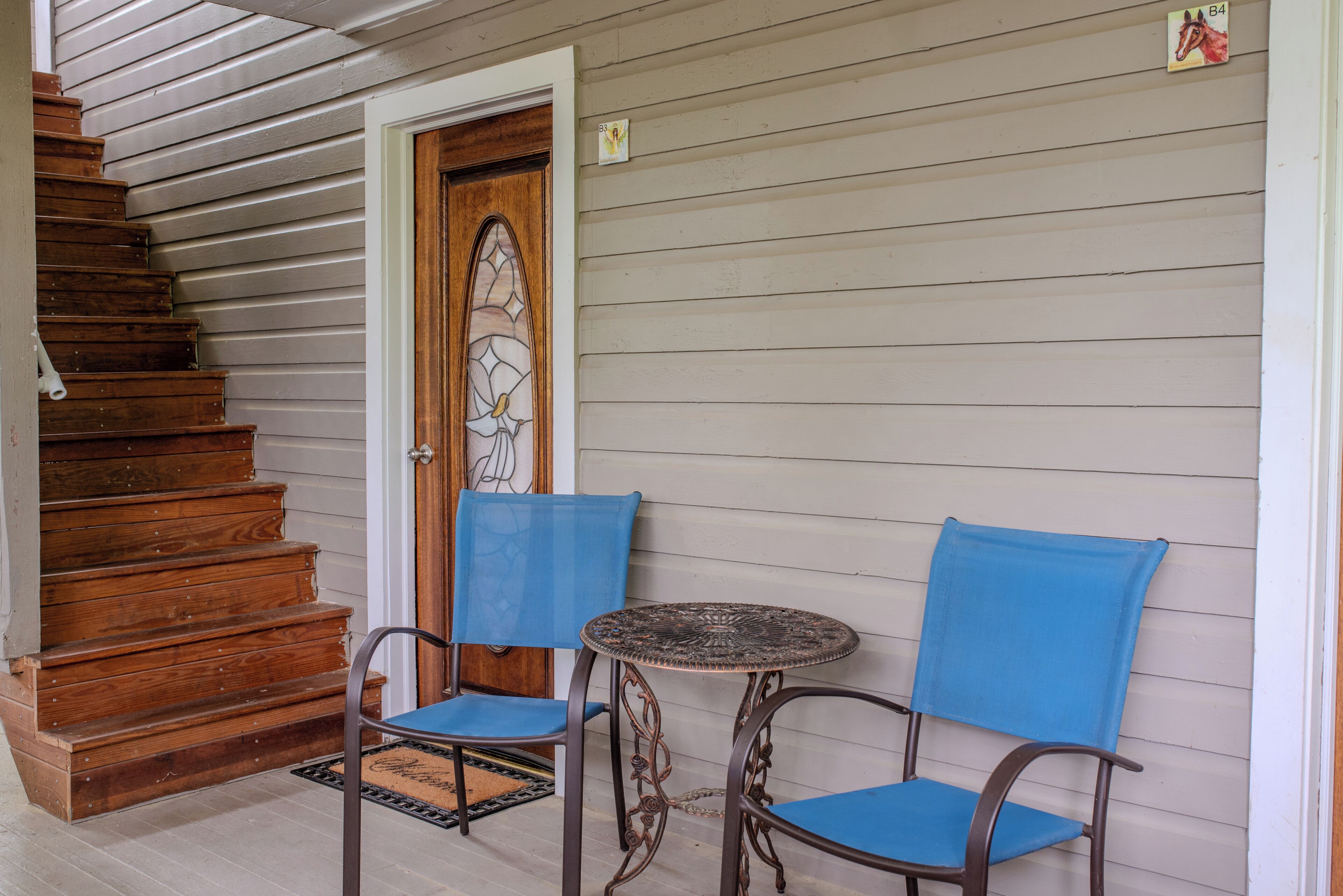 A wooden staircase leading to a door with a stained glass window, two blue chairs, and a small round table.