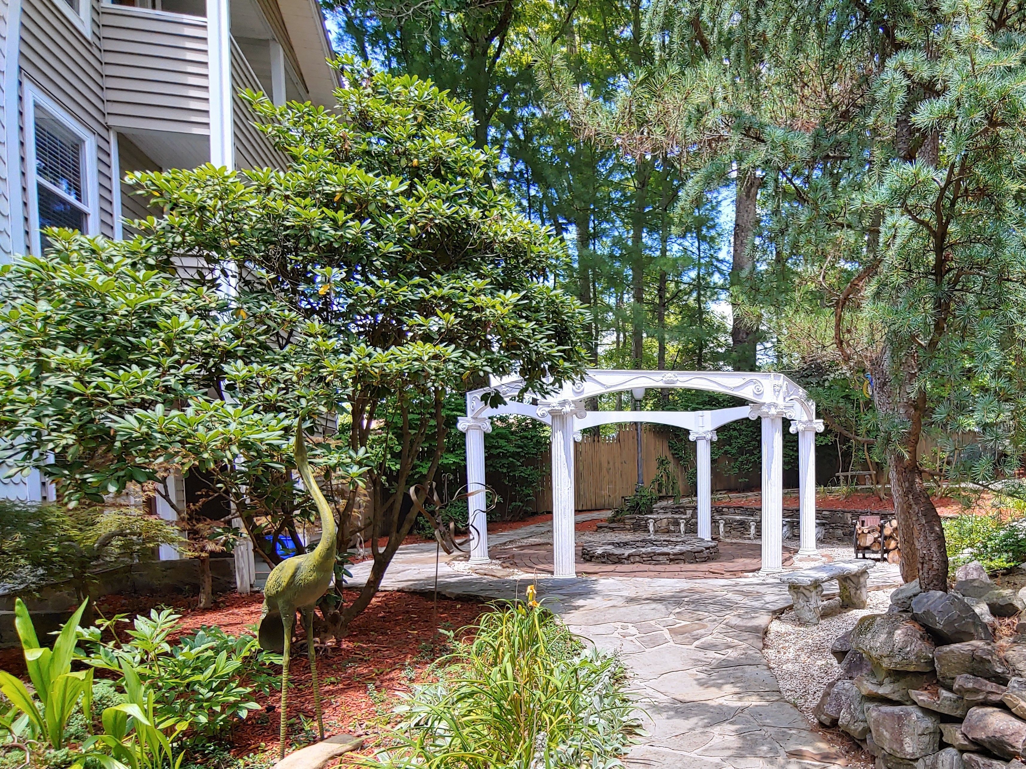 A garden with a white pergola, stone pathway, and various plants.