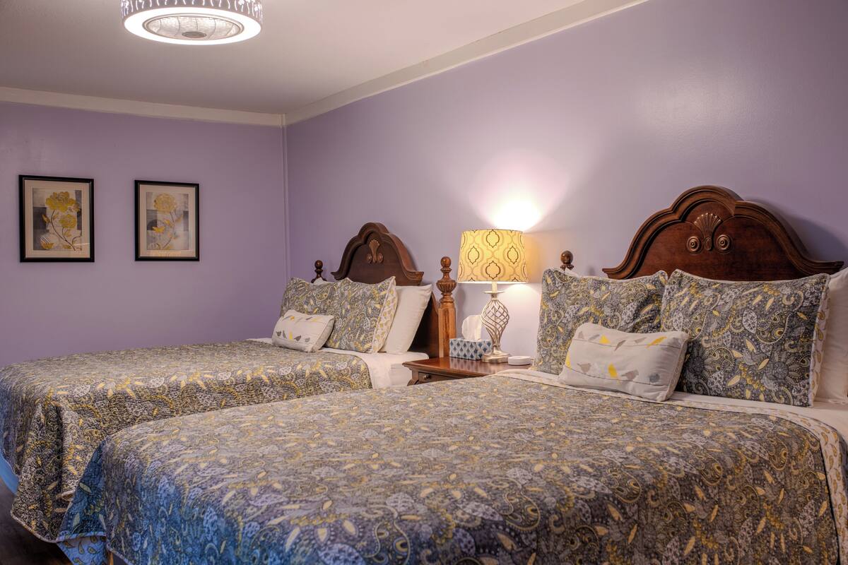 A room with two beds, a nightstand, a lamp, and framed artwork on the wall.