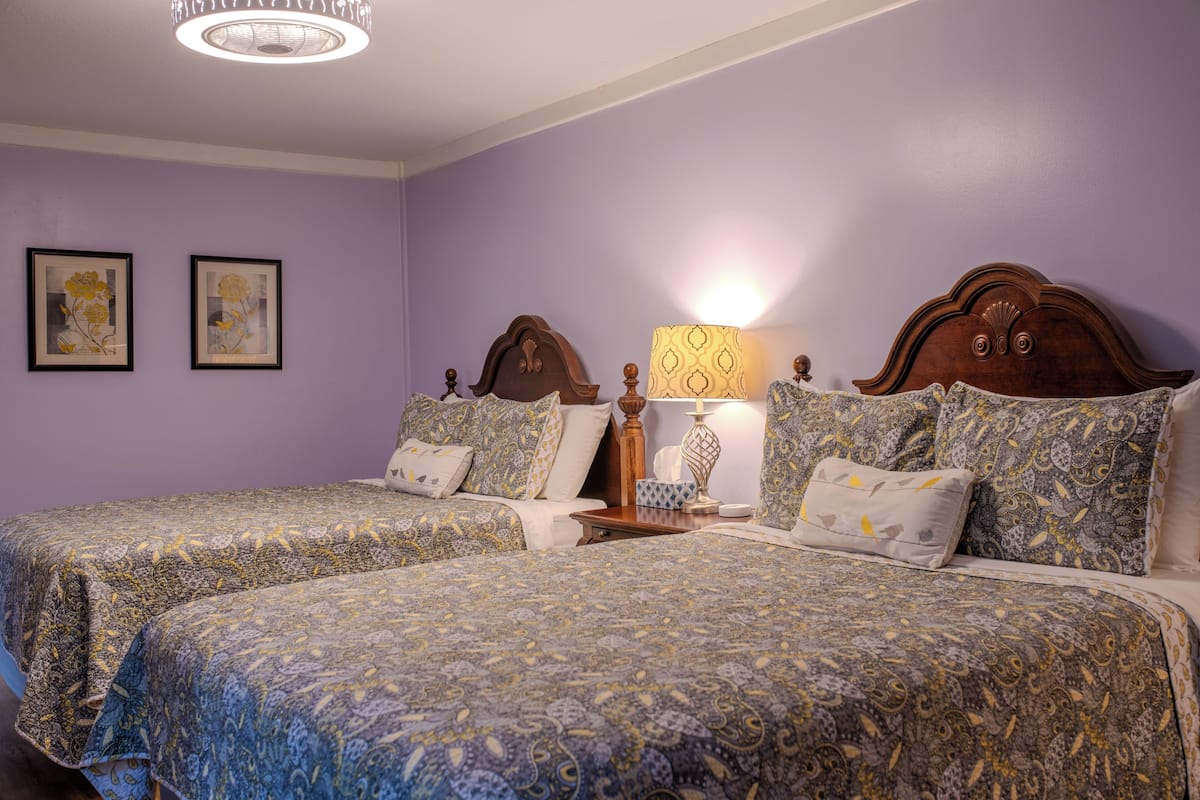 A room with two beds, a nightstand, a lamp, and framed artwork on the wall.