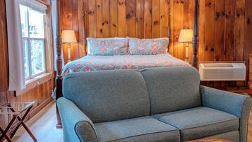A bedroom with a bed, two bedside lamps, a wooden headboard, a window with curtains, and a wooden floor.