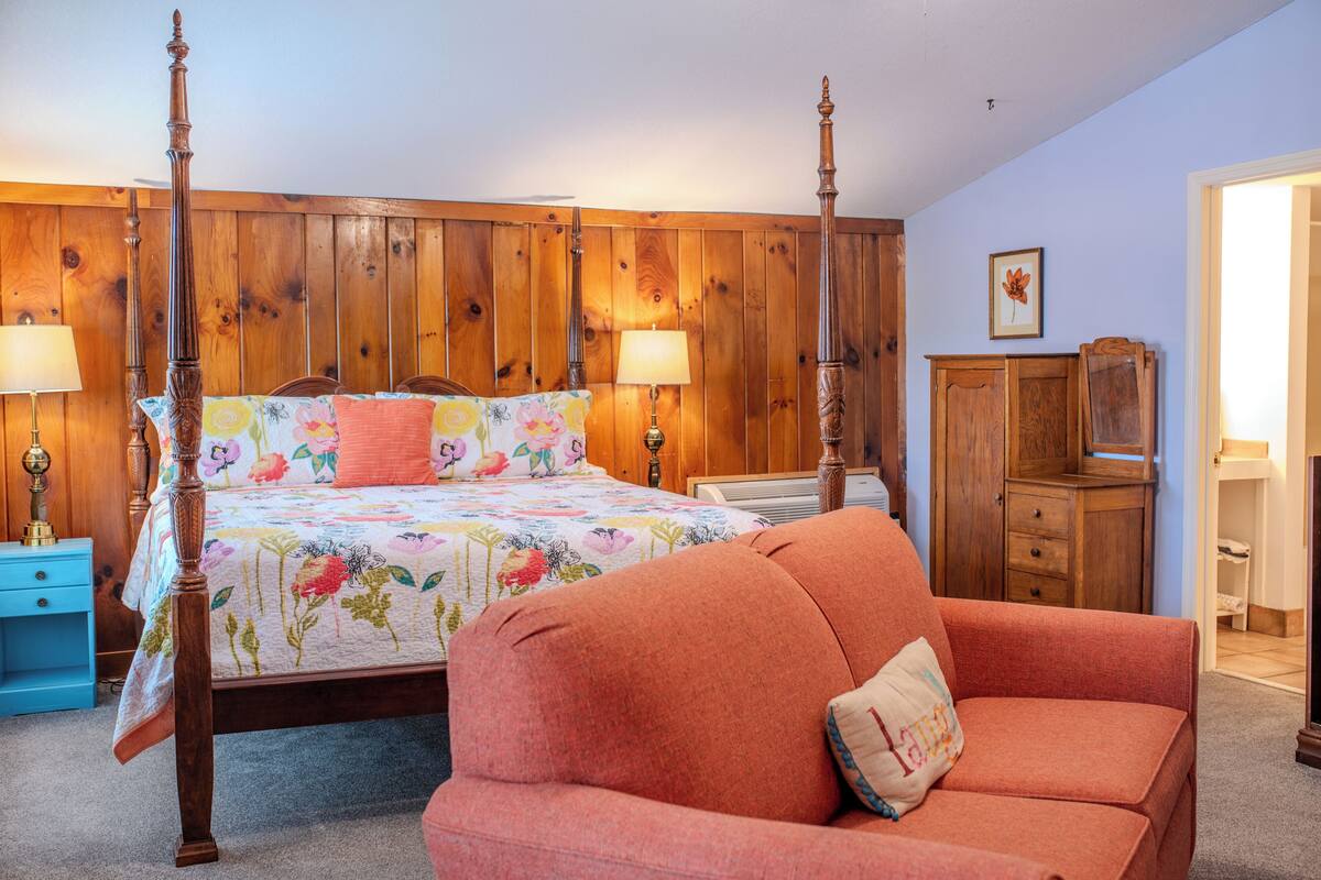 A bedroom with a four-poster bed, a wooden wardrobe, a nightstand, and a sofa.