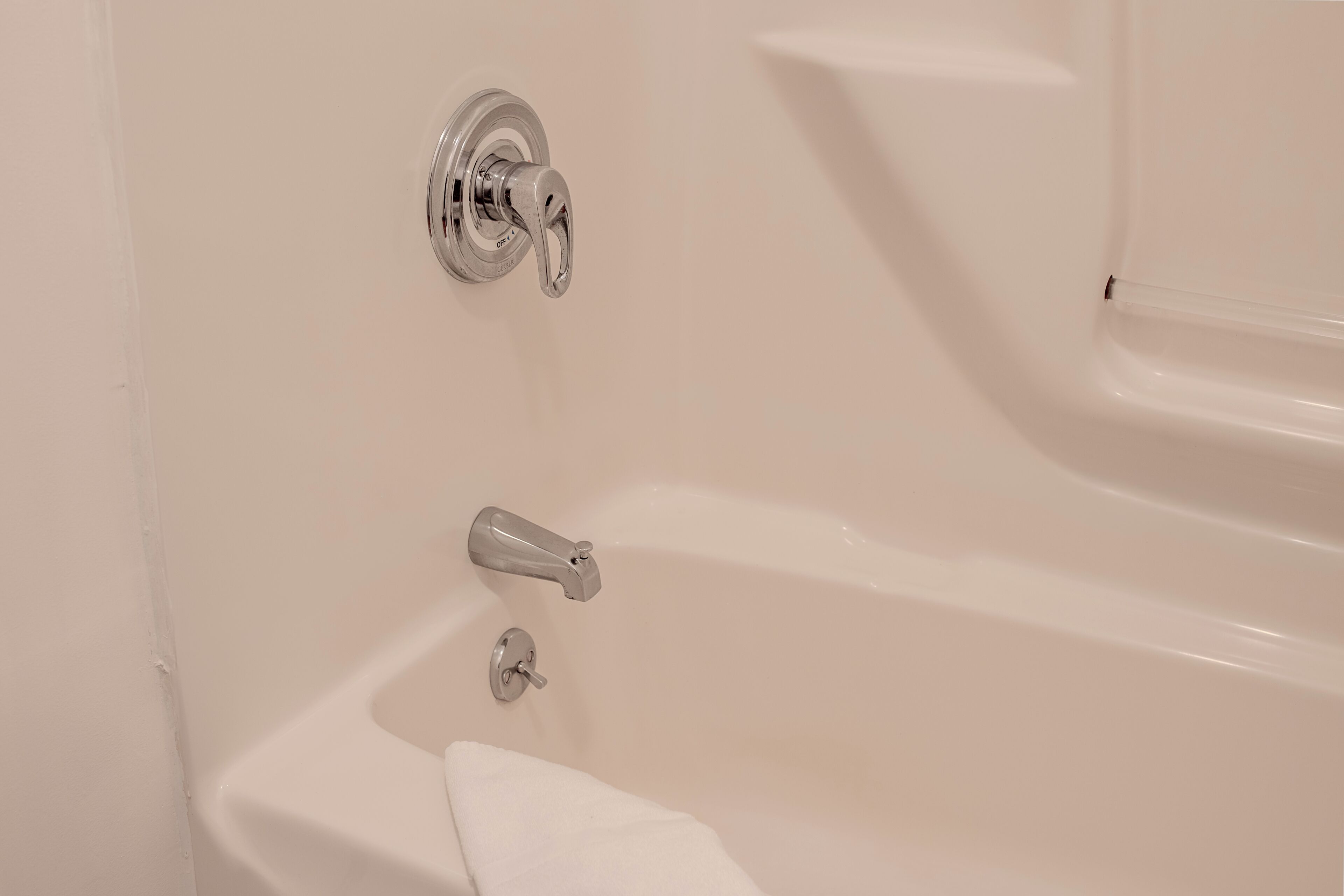 A white bathtub with a faucet and a control knob, a towel on the edge, and a wall-mounted showerhead.
