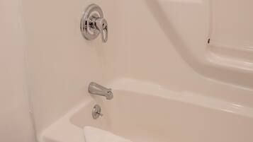 A white bathtub with a faucet and a control knob, a towel on the edge, and a wall-mounted showerhead.