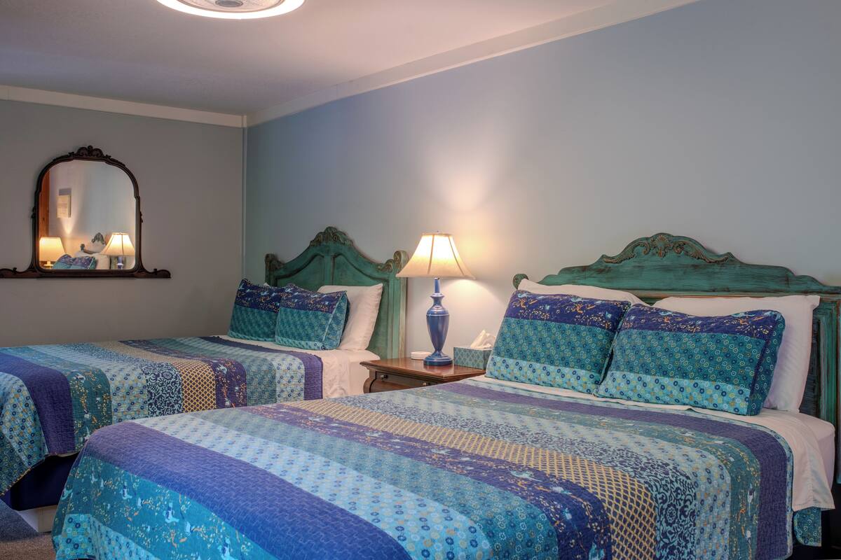 A bedroom with two beds, a nightstand, a lamp, and a mirror.