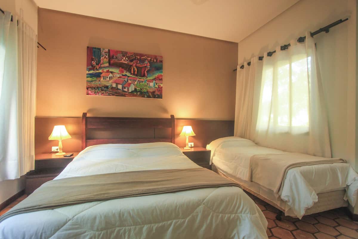 A hotel room with two beds, a painting on the wall, and a window with curtains.