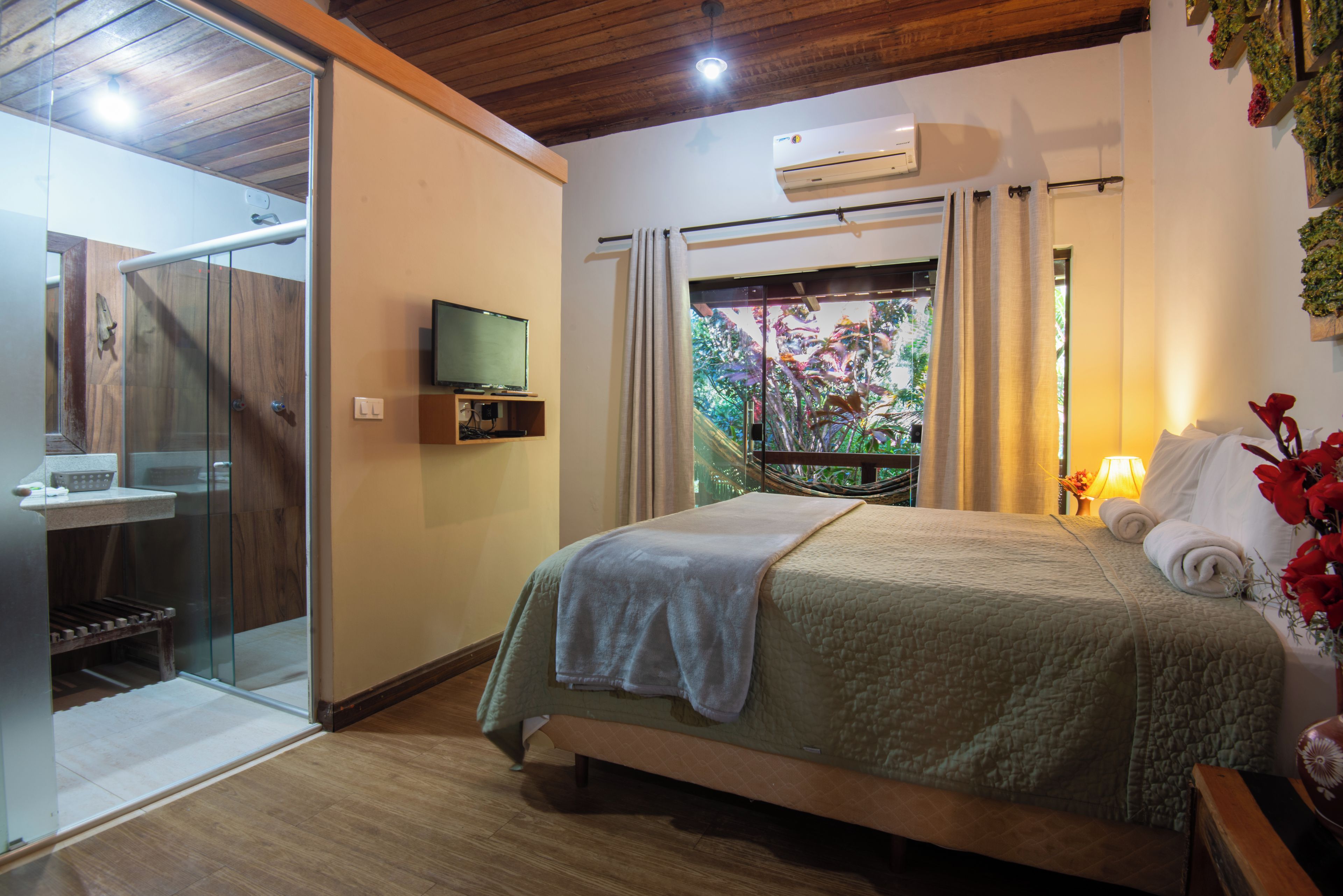 A hotel room with a bed, a television, a shower, and a view of a garden.