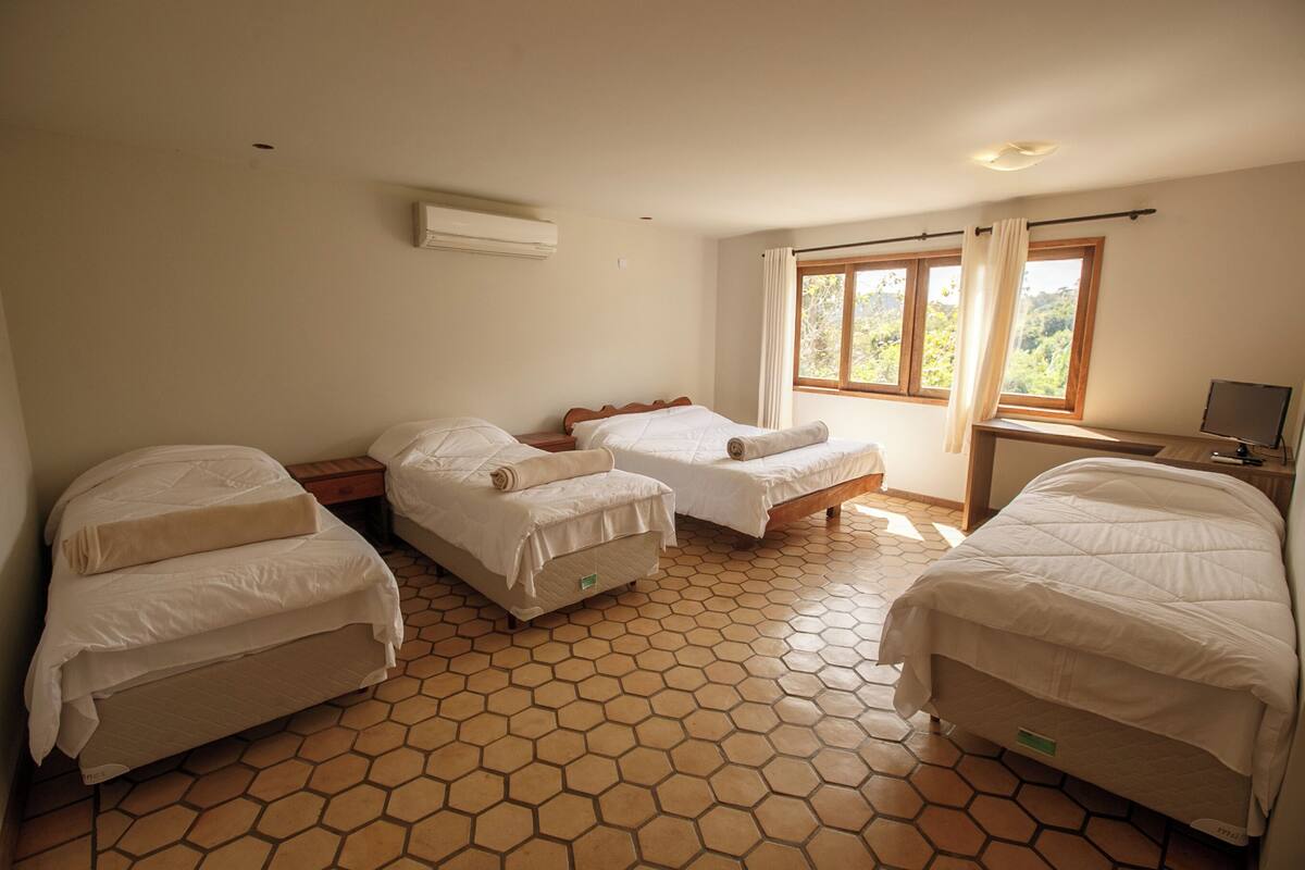 A room with three beds, a TV, and a window with curtains.