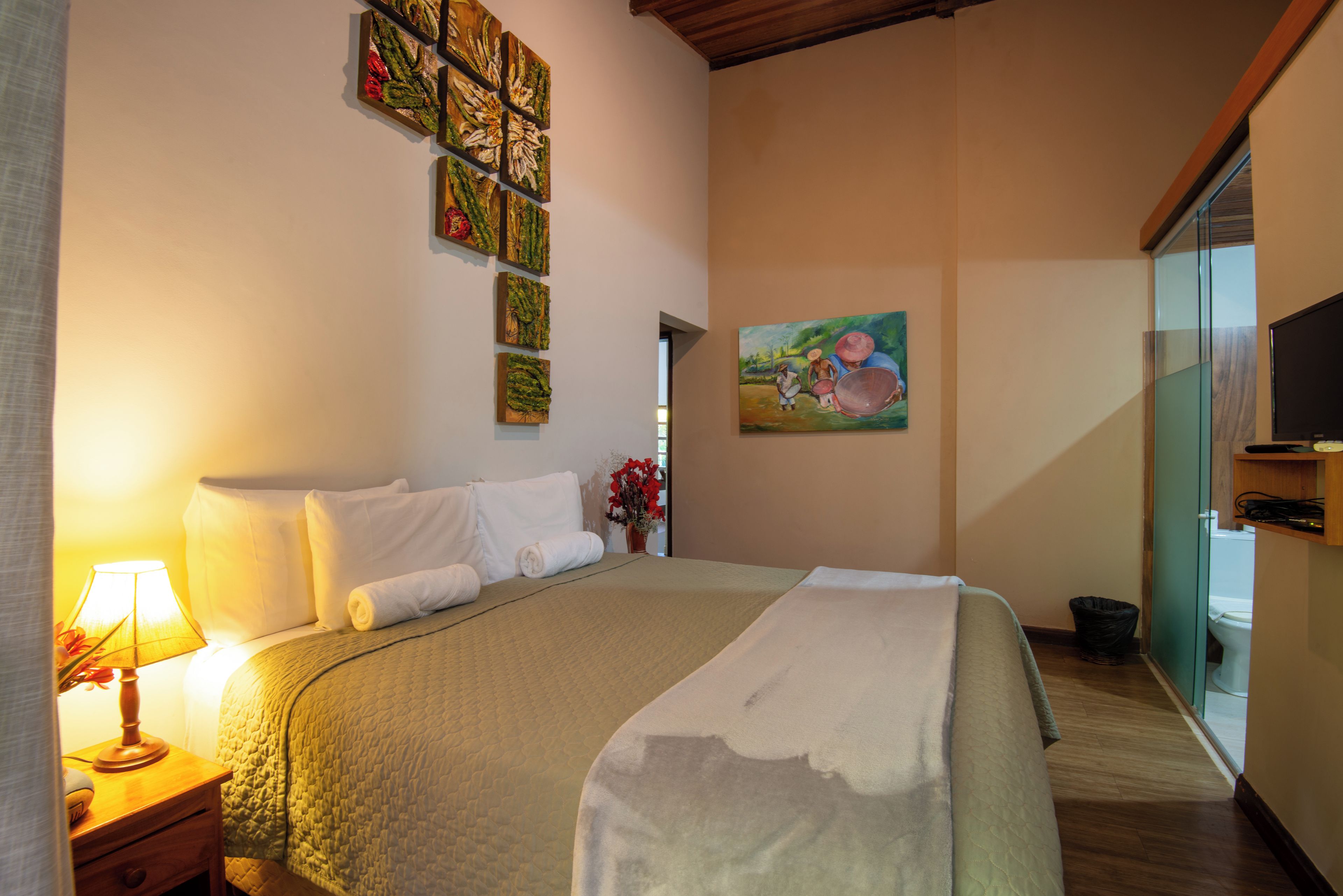 Habitación de hotel con cama, mesita de noche, lámpara, un cuadro y vistas al exterior.