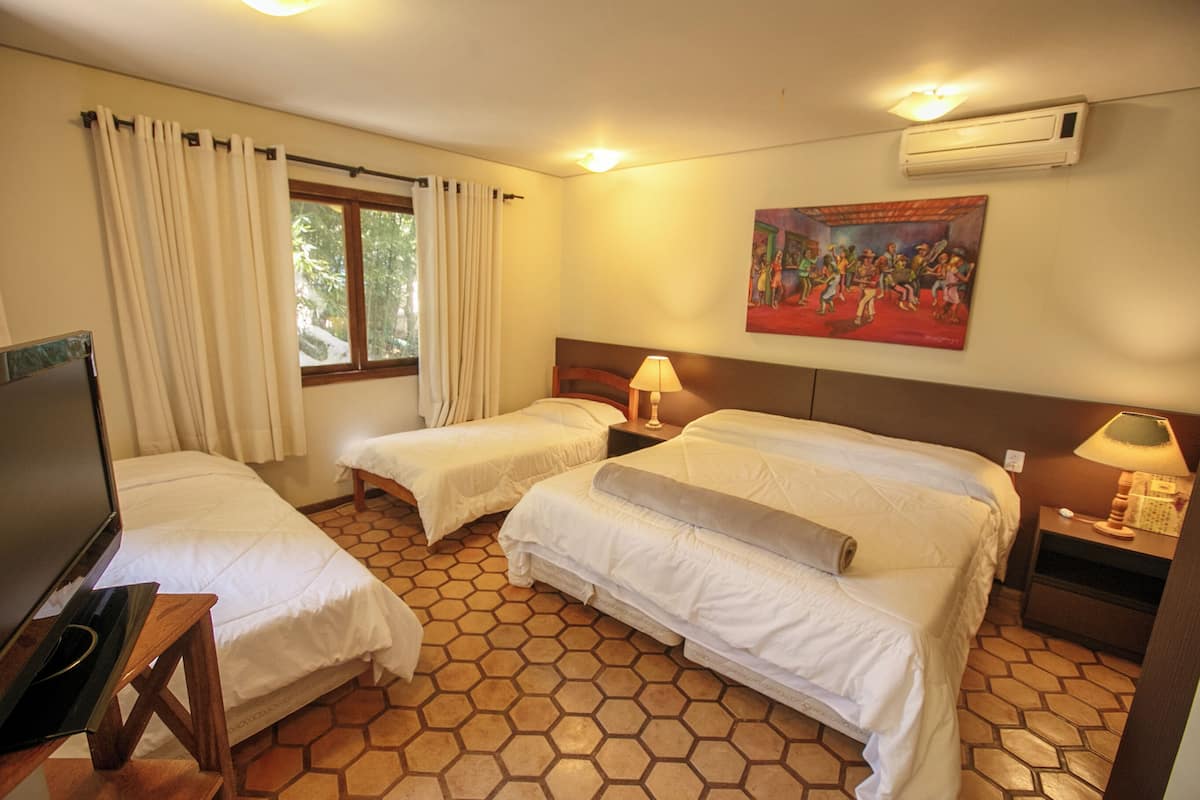 A hotel room with two beds, a TV, a painting on the wall, and a window with curtains.