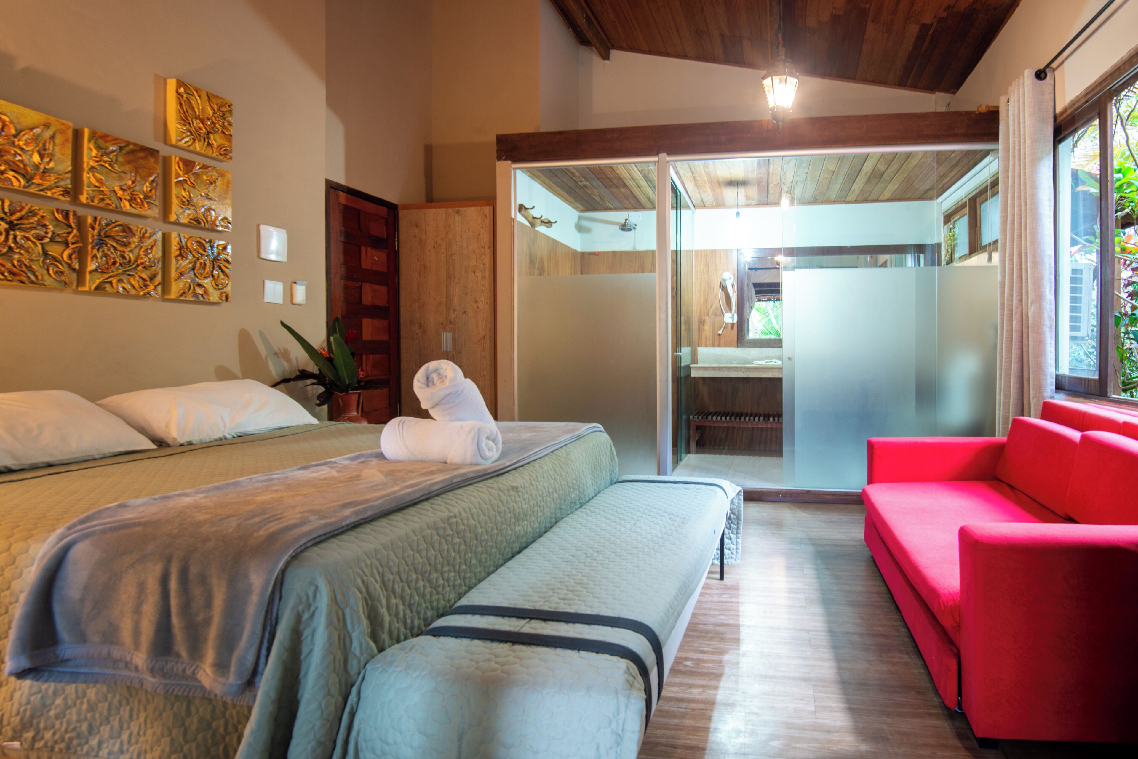 Una habitación de hotel con cama, un banco, un sofá rojo y una puerta corredera que da a un baño.