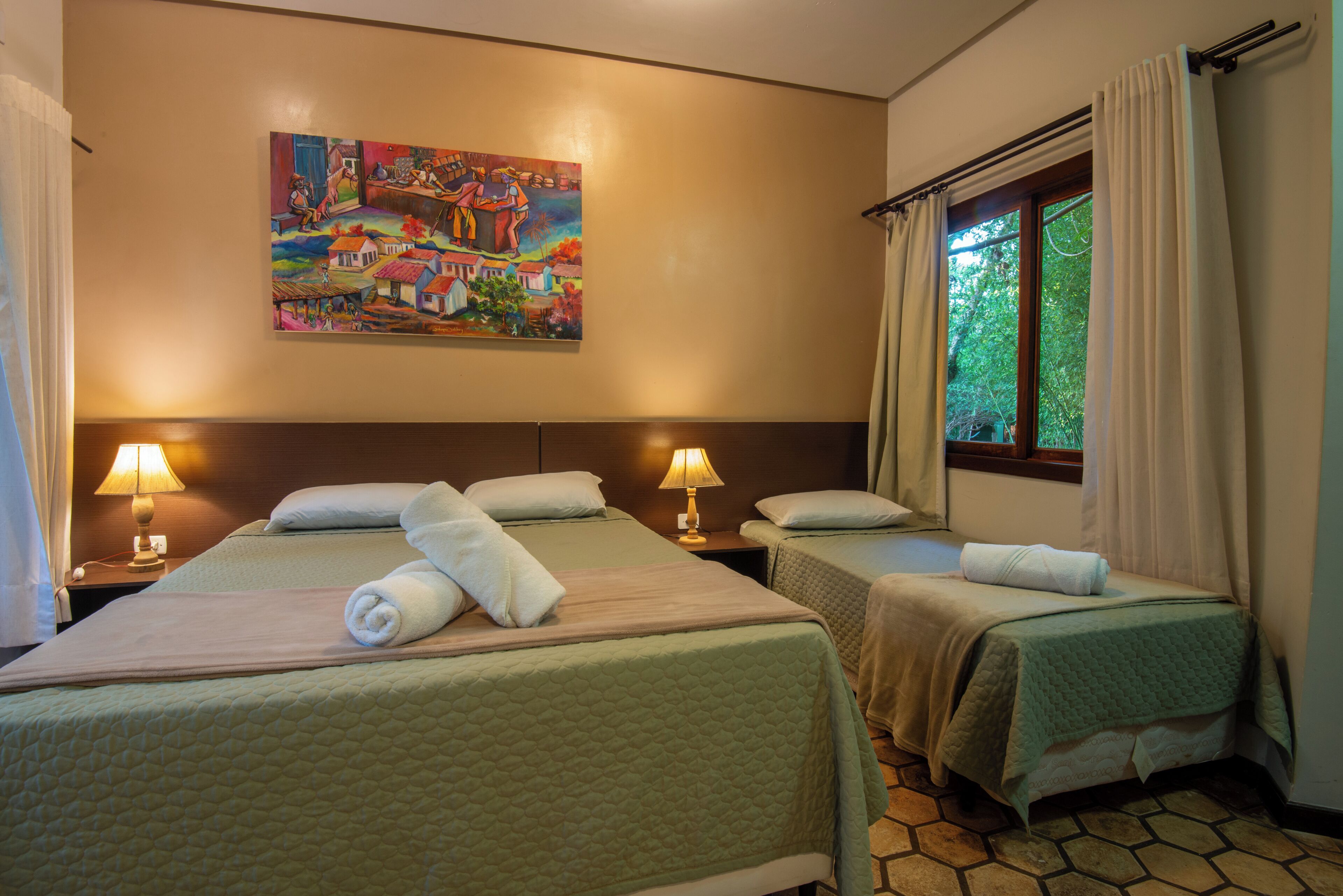 A hotel room with two beds, a painting on the wall, and a window with curtains.