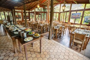 A dining area with hexagonal tiled flooring, wooden tables and chairs, and a buffet setup with various food items. - Pousada Lendas do Capão (Palmeiras)