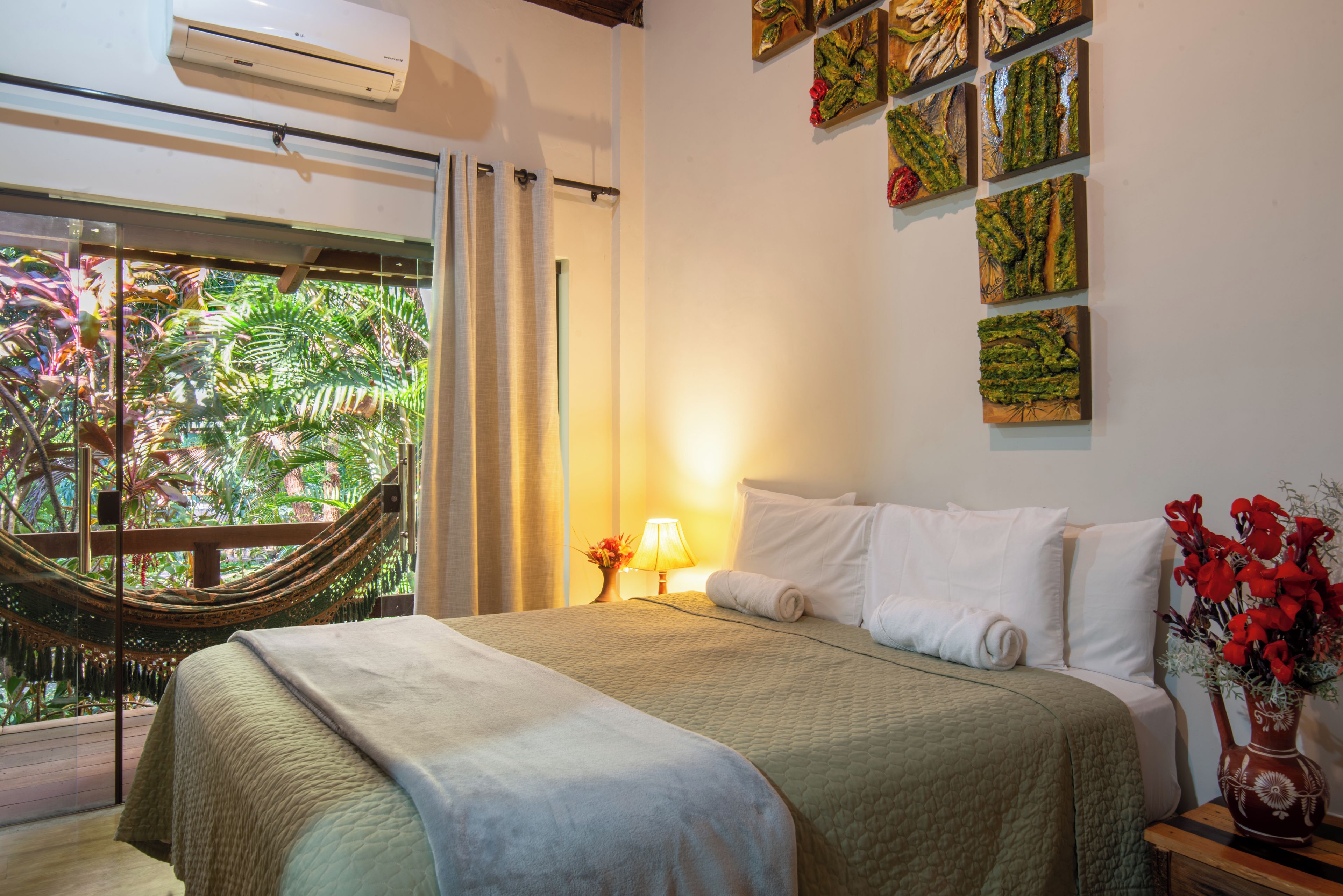 Een hotelkamer met een bed, een hangmat, een raam met uitzicht op groen en wanddecoratie.