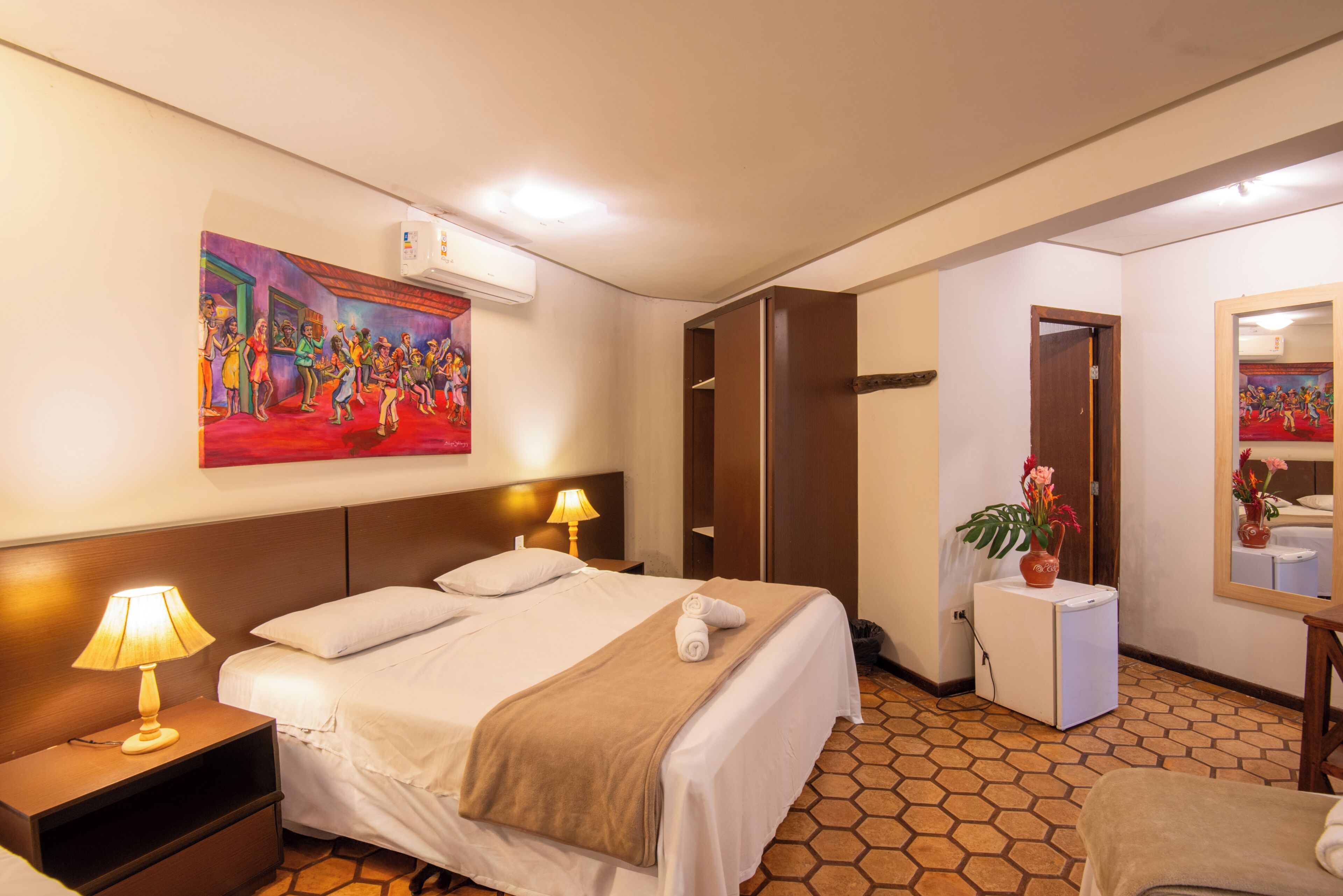 Een hotelkamer met een bed, bedlampen, een schilderij, een spiegel en een kleine plant.