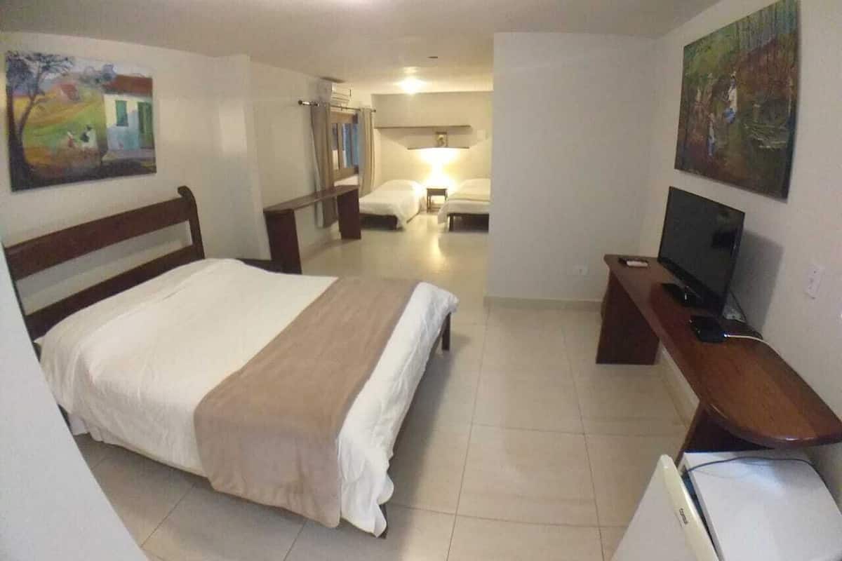 A hotel room with a large bed, a desk with a computer, a television, and artwork on the walls.
