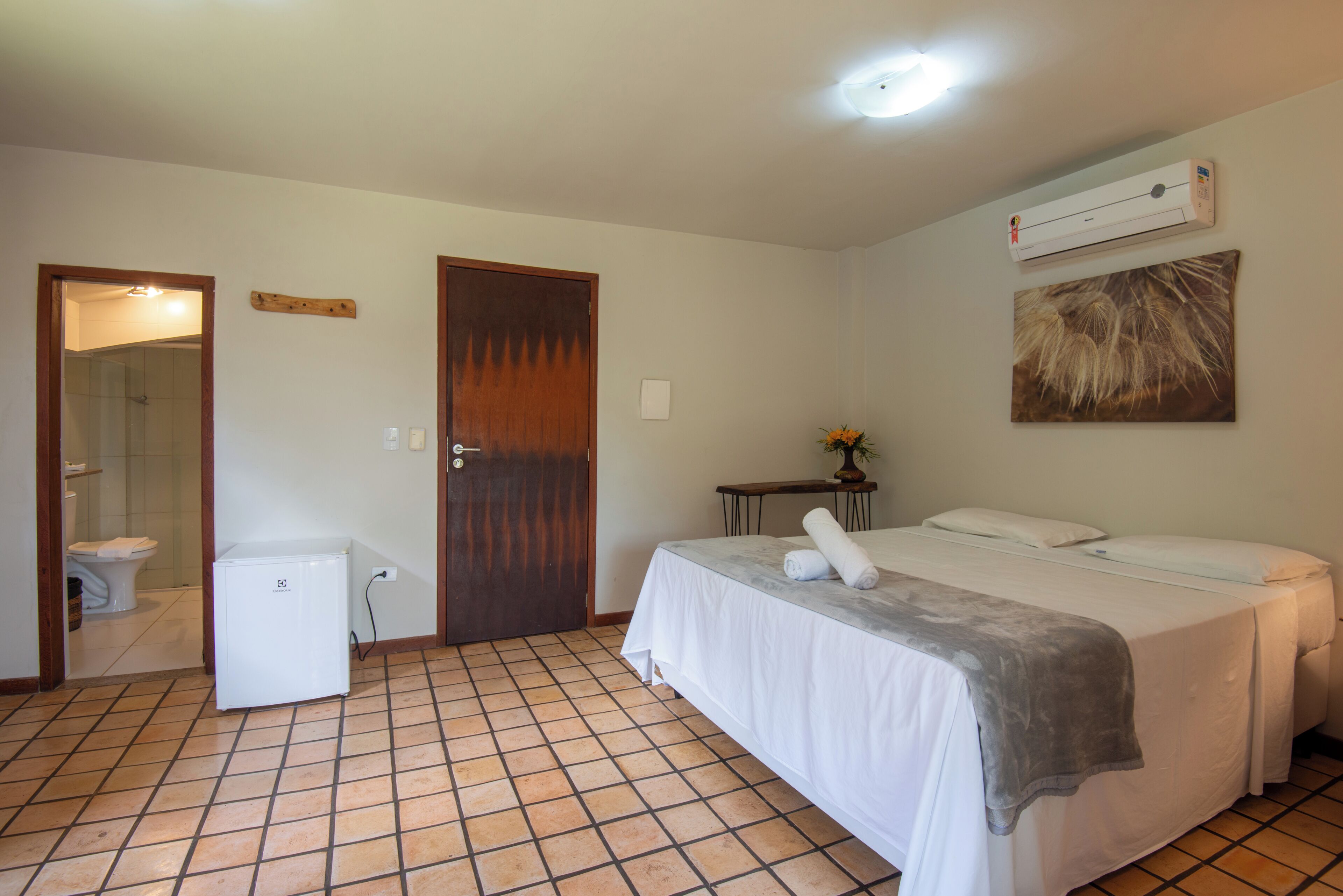 A hotel room with a bed, a small table, a wall-mounted air conditioner, and a shower area.