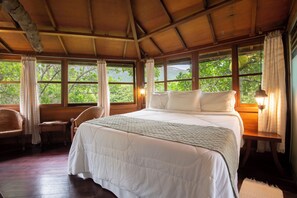 A room with a large bed, wooden walls, and windows overlooking greenery. - Pousada Lendas do Capão (Palmeiras)