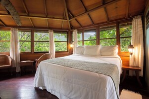 A room with a large bed, wooden walls, and windows overlooking greenery.