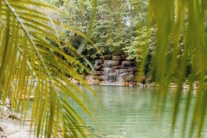 A waterfall cascading over a rocky ledge into a calm pond, surrounded by dense greenery. - Pousada Lendas do Capão (Palmeiras)