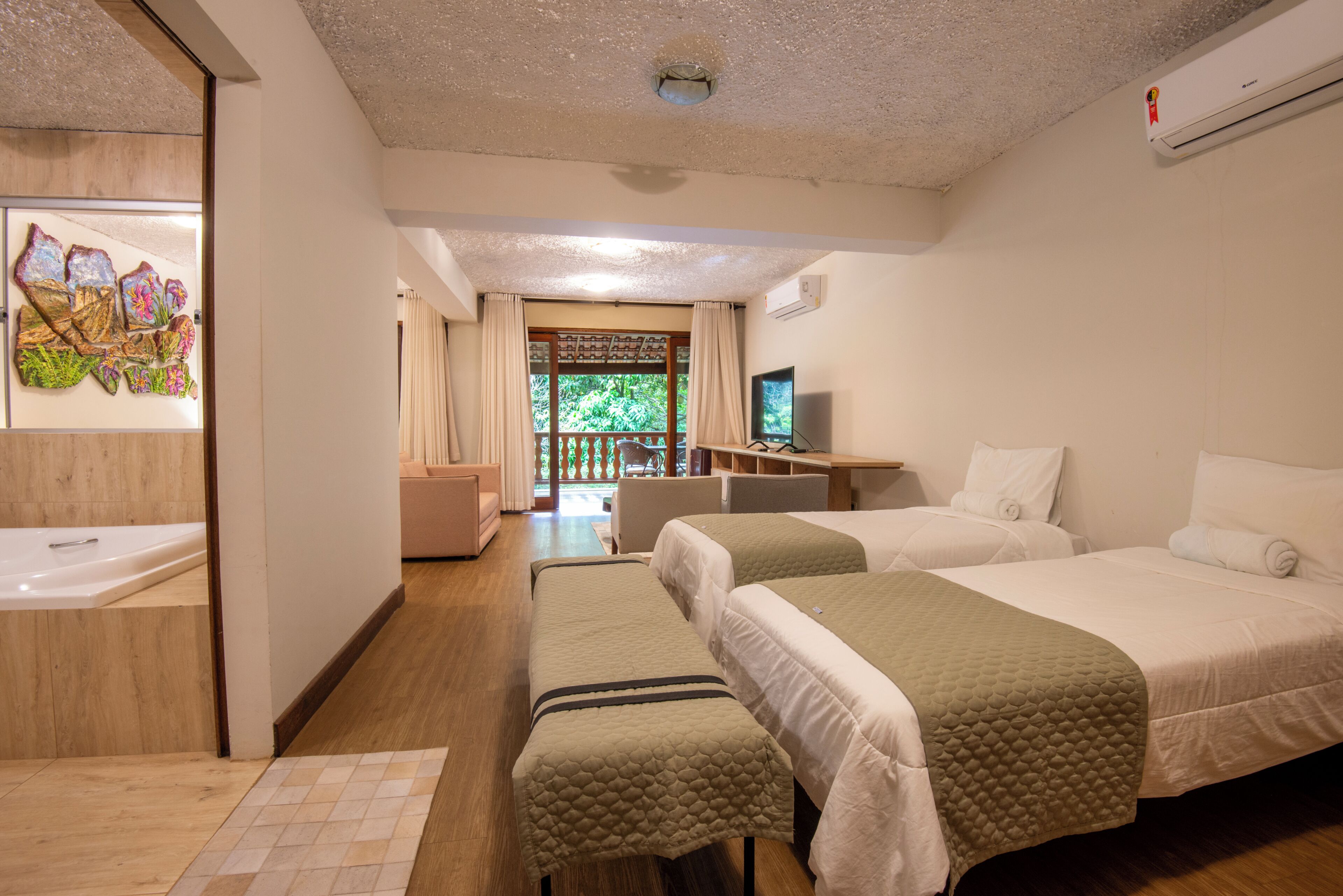 A hotel room with two beds, a desk with a computer, a TV, and a bathroom with a shower and a bathtub.