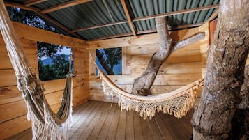 A wooden cabin with a hammock suspended from a tree, wooden floors, and a corrugated metal roof.