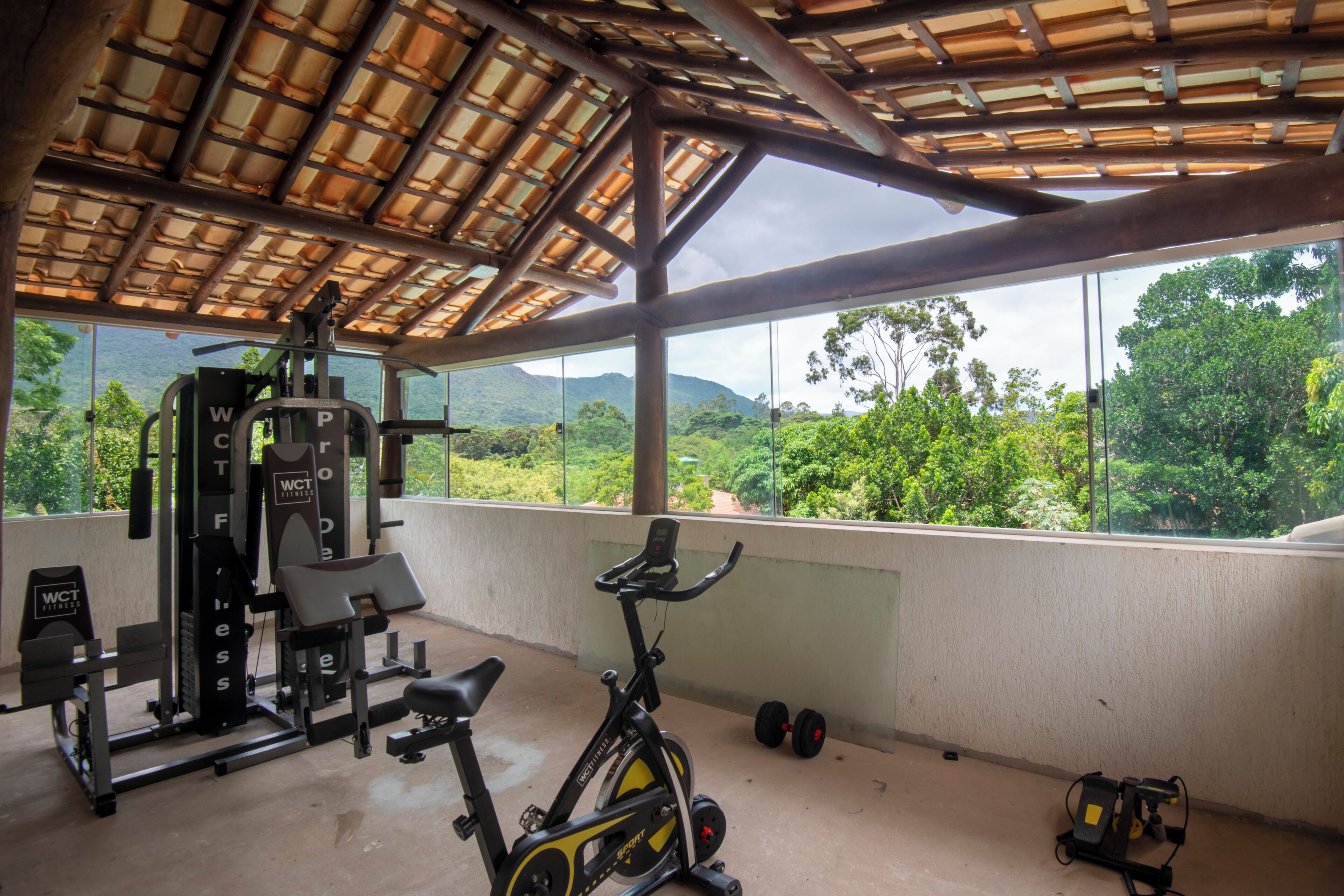 Een fitnessruimte met trainingsapparatuur, een hometrainer en uitzicht op een bergachtig landschap door grote ramen.