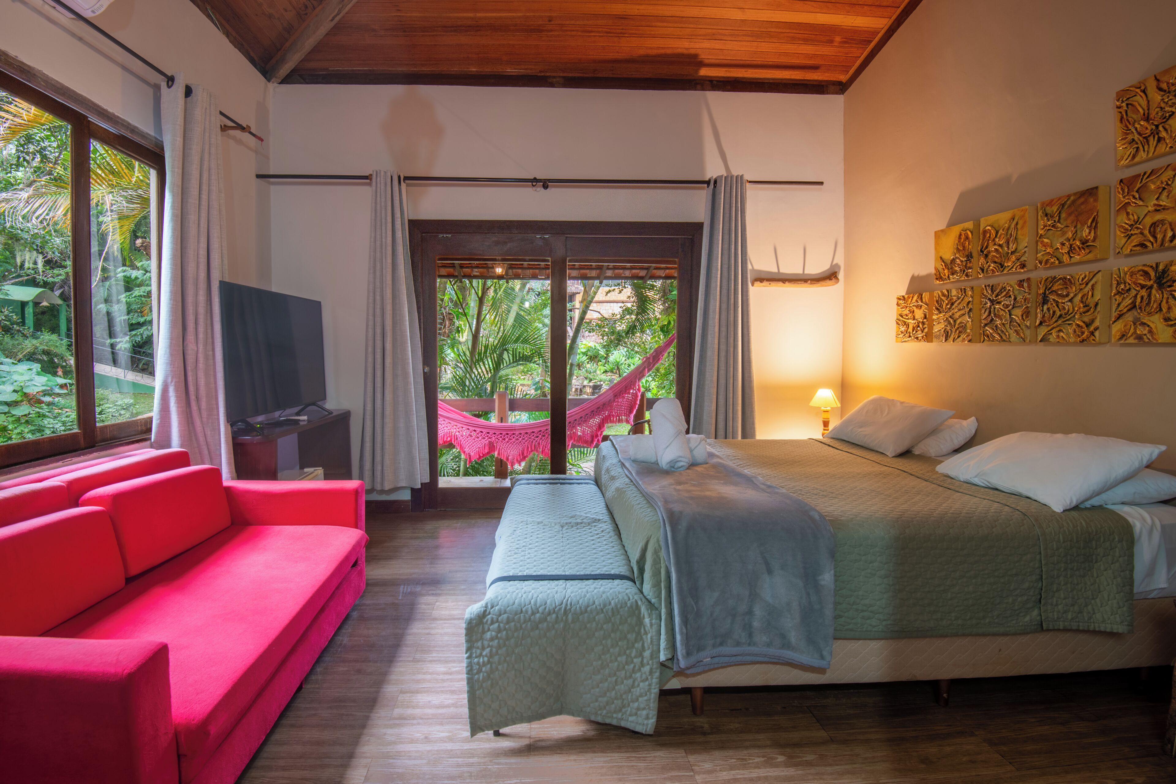 A bedroom with a bed, a red sofa, a television, and a hammock.