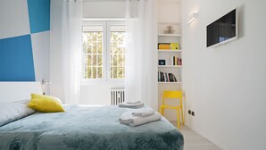 Un dormitorio con cama, ventana, estantería y televisor.