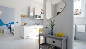 Una cocina moderna con armarios blancos, horno integrado y una zona de comedor con mesa consola gris.