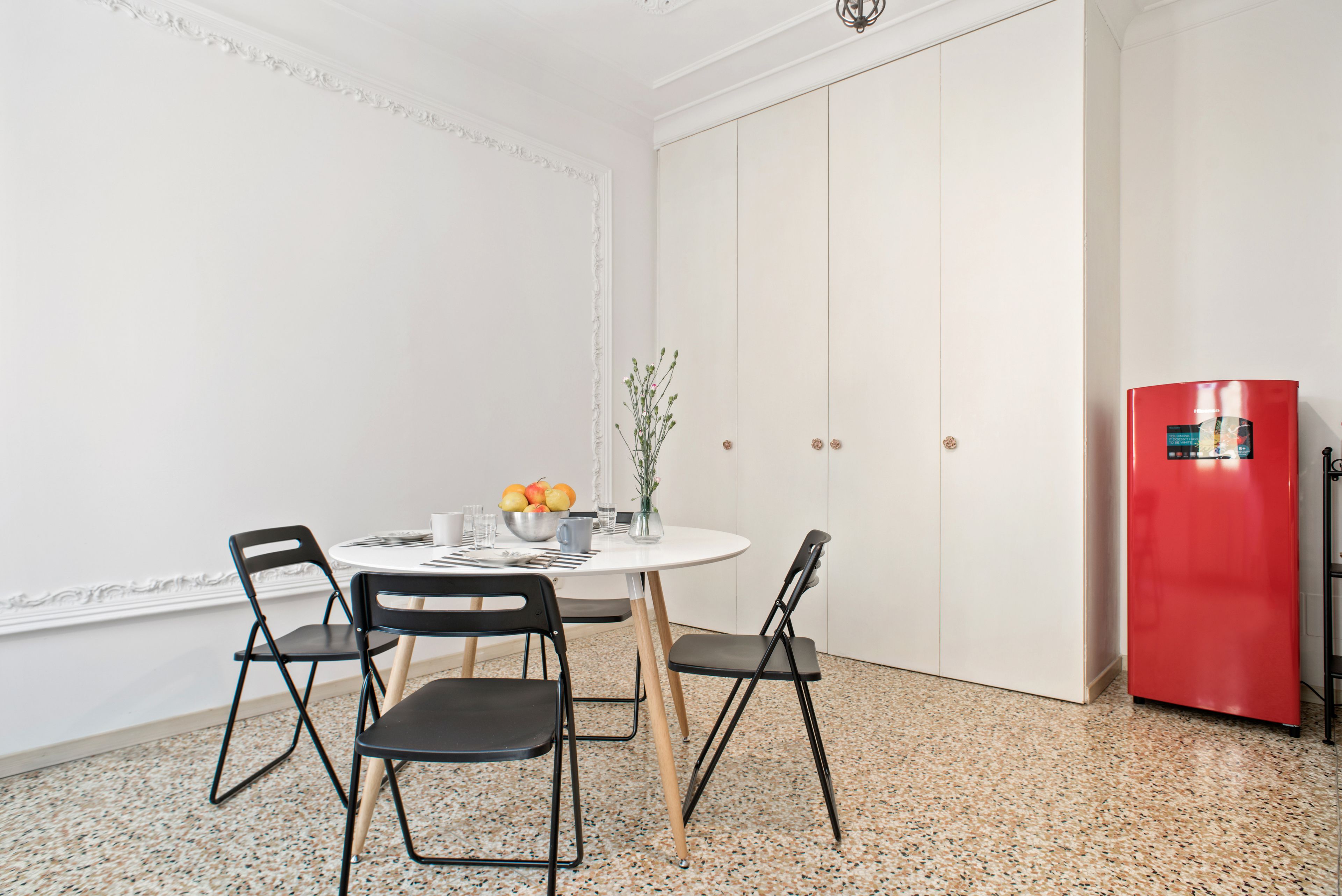 Un coin repas comprenant une table ronde, quatre chaises, un réfrigérateur rouge et un meuble blanc.