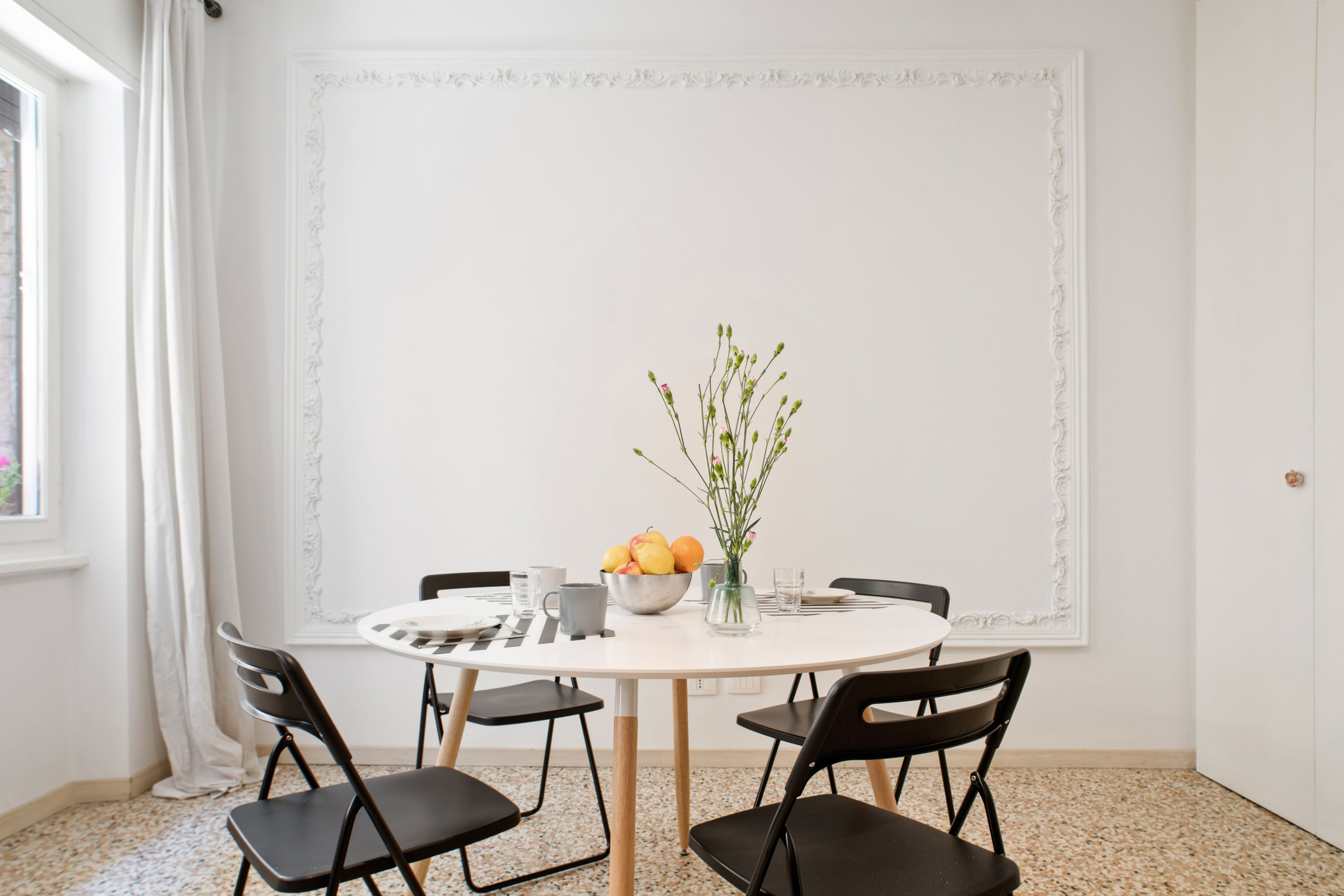 A round dining table with four chairs, a bowl of fruit, and a vase with flowers.