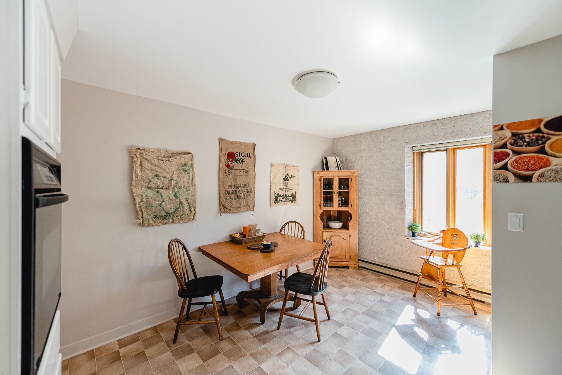 A dining area with a wooden table and chairs, a cabinet with glass doors, and a window with a view of spices.