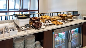 Montaje de bufé con diversos alimentos, una estación de café y un refrigerador con bebidas.
