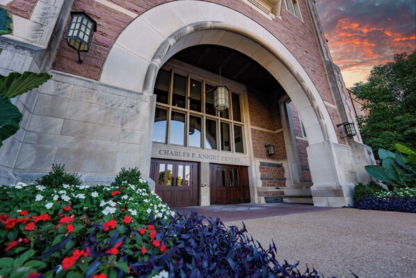 The exterior of the Charles F. Knight Center with a stone facade, large arched entrance, and a sign above the doors. - The Knight Center at Washington University (St. Louis)
